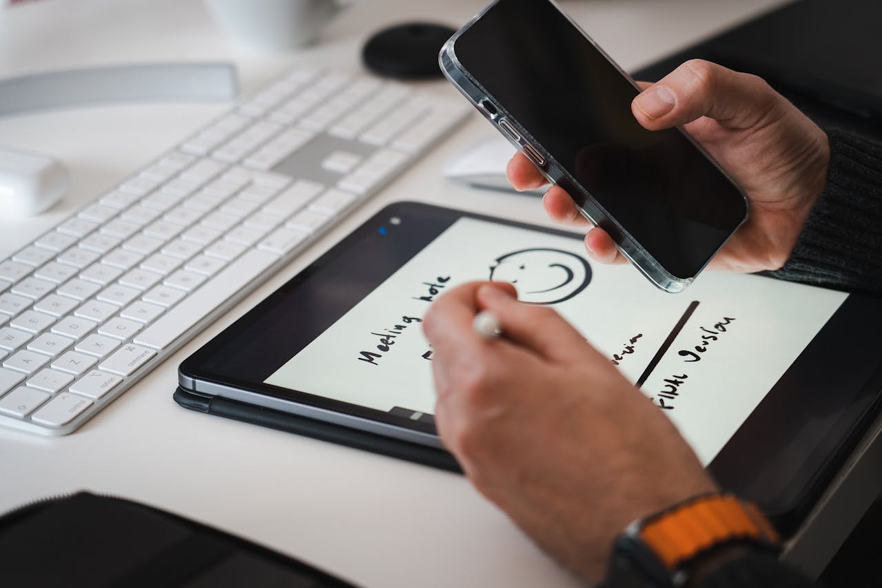 Hands using a stylus on a tablet for note-taking alongside a smartphone, suitable for tech themes.