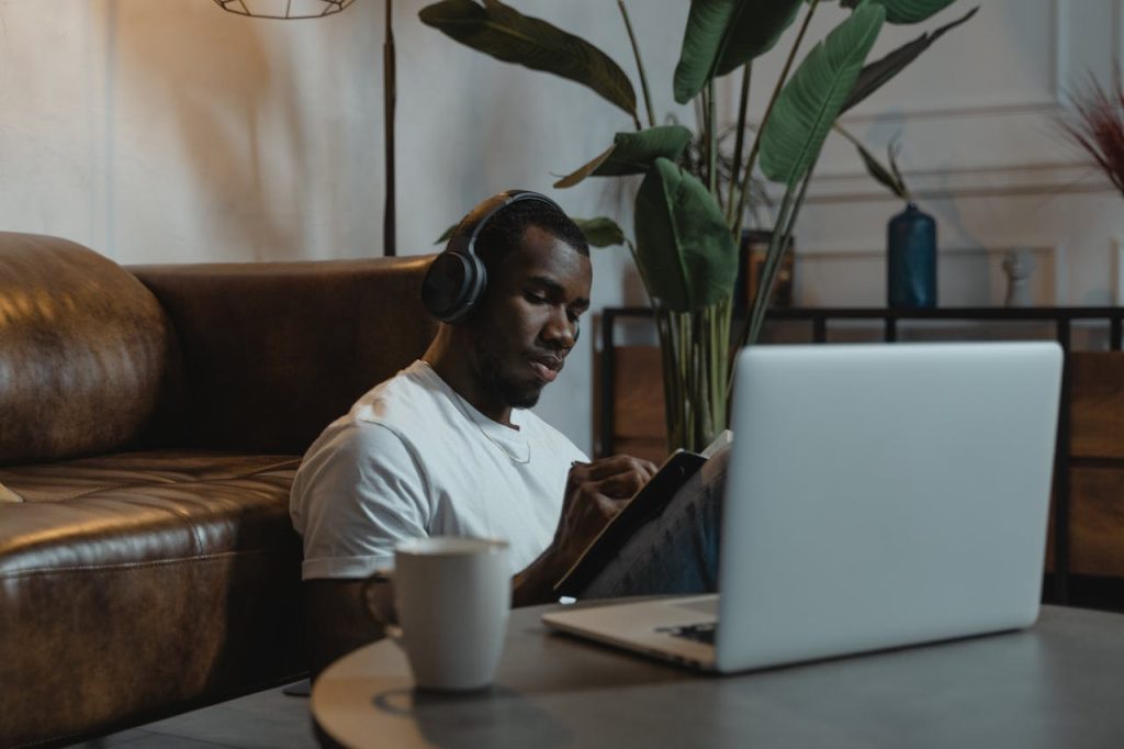 African American man wearing headphones, engaged in online learning at home with a laptop.